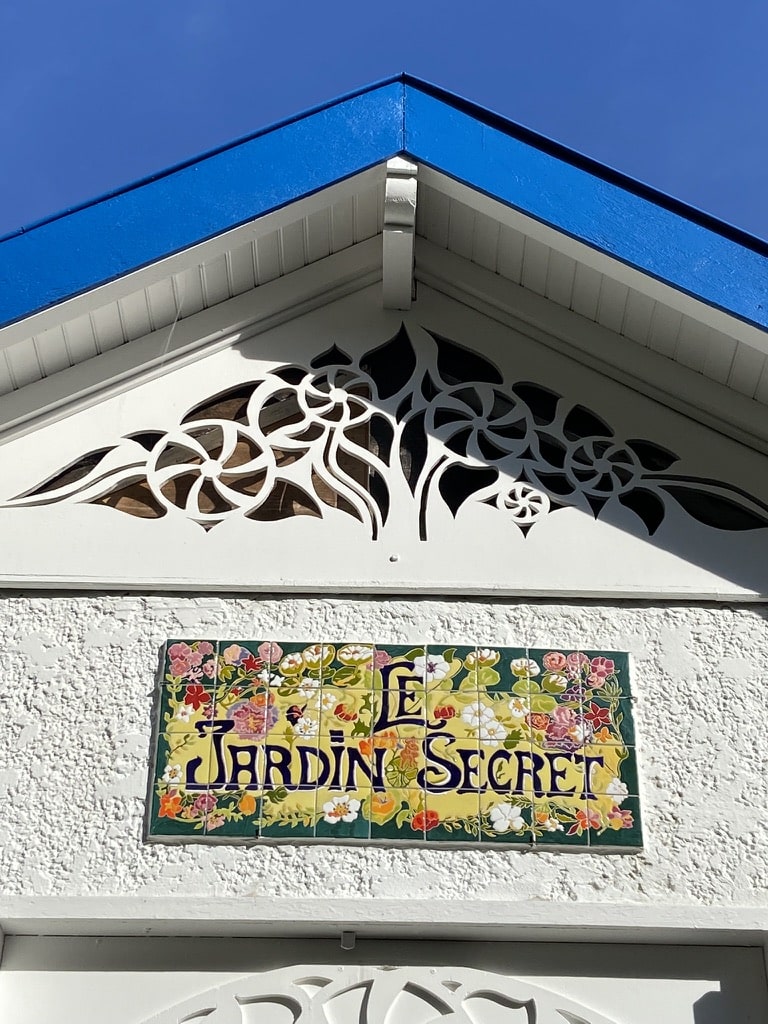 Plaque « Le Jardin Secret » en céramique peinte à la main, au fronton blanc d’une maison sous un toit bleu