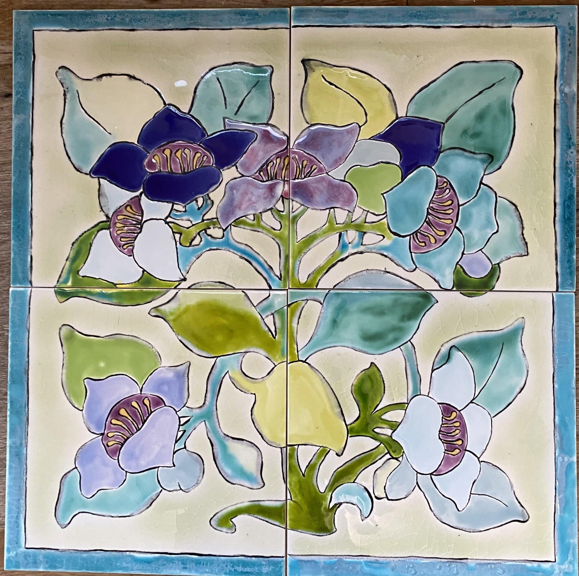 Panneau de quatre carreaux en céramique peints à la main : fleurs bleues, mauves et blanches aux cœurs violets, feuillages verts, bordure turquoise