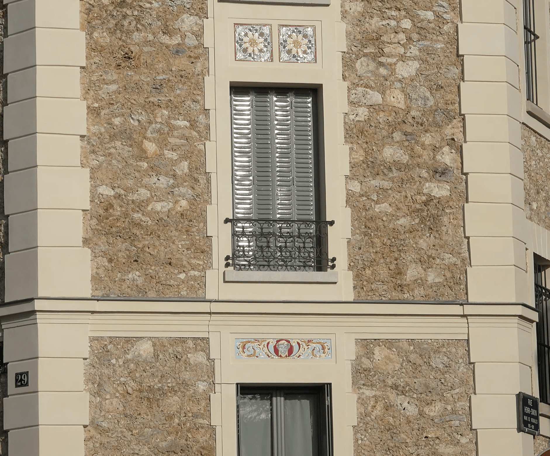 Cabochons floraux Art Nouveau et frise au visage sur façade en pierre meulière, détail rapproché, immeuble Versailles
