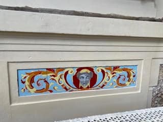 Frise en céramique émaillée représentant un visage féminin entouré d'arabesques dorées et rouges sur fond bleu, réalisée par Laurence Brecher pour un immeuble à Versailles